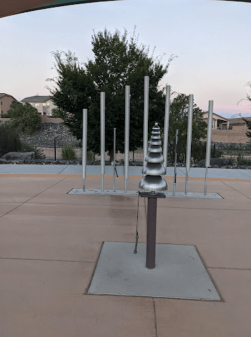 A modern sculpture with a series of vertical poles and a spiral structure in a park setting during twilight.