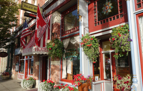 Historic hotel facade with flags, flower baskets, and vibrant storefronts in a charming urban setting.
