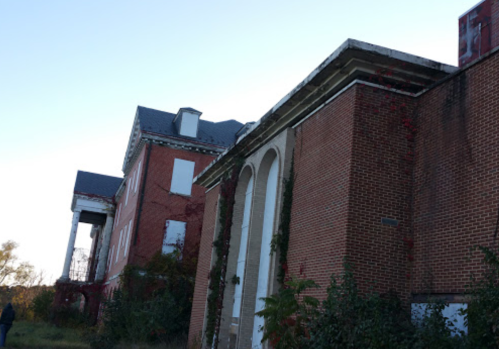 Abandoned brick building with ivy climbing its walls, featuring a large archway and a sloped roof.