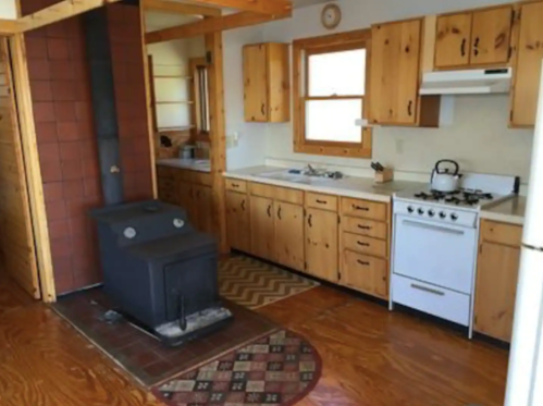 Cozy kitchen with wooden cabinets, a black stove, and a white gas range, featuring a rustic design and warm lighting.
