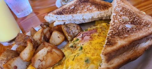 A plate with a fluffy omelet, golden-brown toast, and crispy potato wedges, accompanied by a glass of juice.
