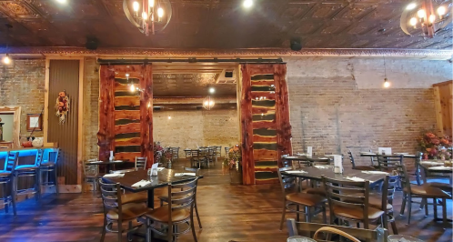 Interior of a rustic restaurant featuring wooden decor, tables, and exposed brick walls with warm lighting.