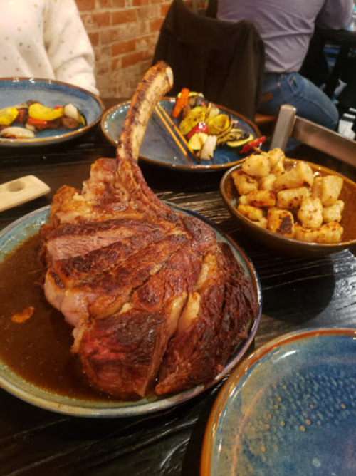 A large, juicy tomahawk steak on a plate, accompanied by roasted potatoes and colorful grilled vegetables.