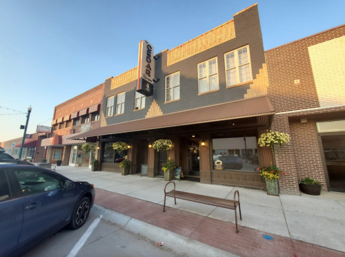 A historic building with a sign, large windows, and flower planters, located on a sunny street.
