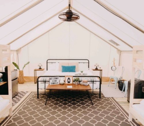 Cozy glamping tent interior with a double bed, bunk beds, and stylish decor, featuring a rug and plants.