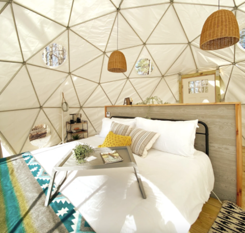 Cozy interior of a geodesic dome with a bed, decorative pillows, a tray, and hanging light fixtures.