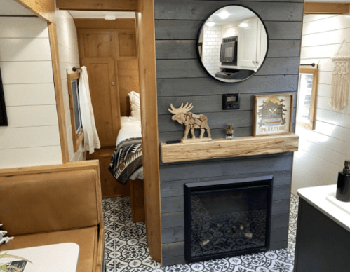 Cozy interior of a tiny home featuring a fireplace, circular mirror, and rustic decor with a moose figurine.