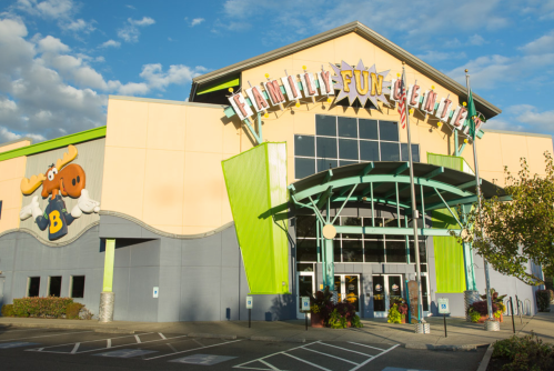 Exterior of a colorful family fun center with a large sign, featuring a moose mascot and a bright blue sky.