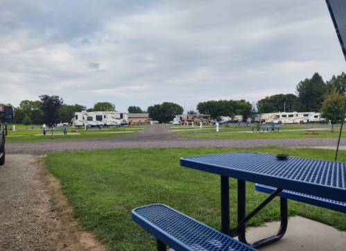 A view of a campground with RVs parked, grassy areas, and picnic tables under a cloudy sky.