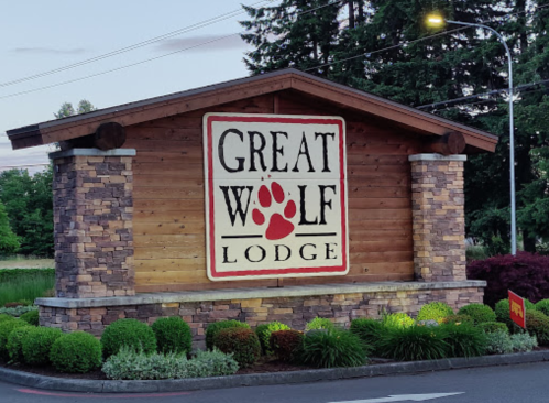 Sign for Great Wolf Lodge featuring a wooden structure and stone accents, surrounded by greenery.