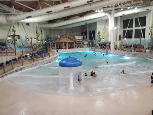 Indoor water park scene with a wave pool, water features, and people enjoying the water. Bright and spacious atmosphere.