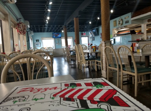 Interior of a casual restaurant with empty tables, a pizza box in the foreground, and TVs on the walls.
