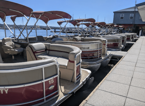 A row of parked pontoon boats with red canopies along a waterfront dock on a sunny day.