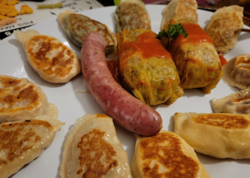 A plate of assorted dumplings, including fried dumplings, stuffed cabbage rolls, and a sausage, garnished with parsley.