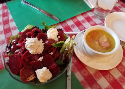 A colorful salad with beets and cheese, alongside a bowl of soup on a checkered tablecloth.