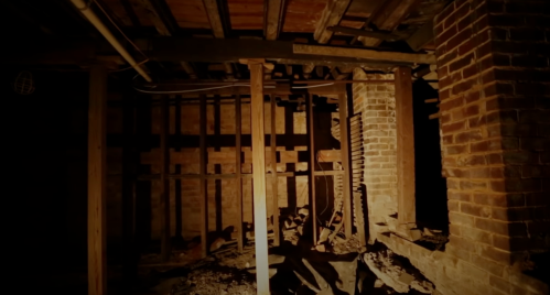 Dimly lit basement with exposed brick walls, wooden beams, and scattered debris on the floor.