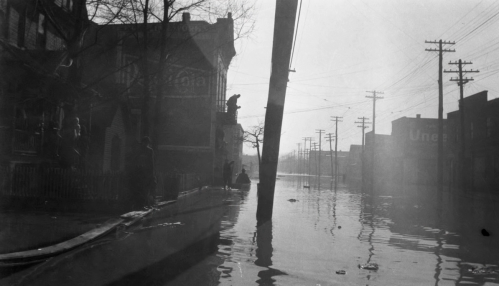 A flooded street with submerged buildings and a utility pole, shrouded in mist and shadows.
