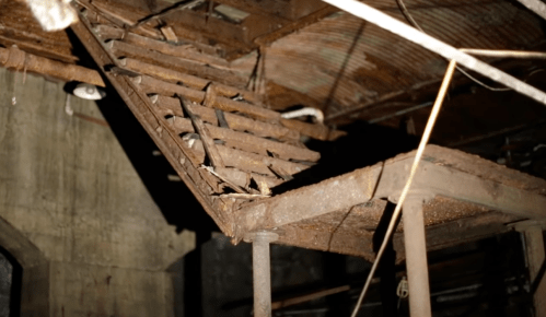 A dilapidated wooden staircase in an abandoned building, with rusted metal supports and a dark, eerie atmosphere.