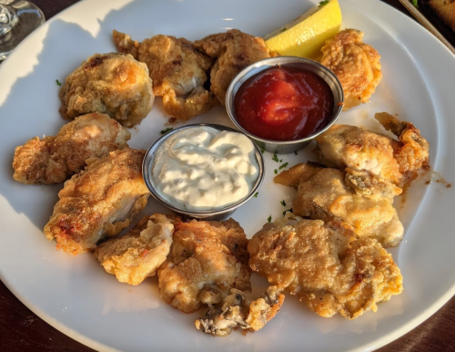 A plate of fried oysters with dipping sauces, including cocktail sauce and tartar sauce, garnished with a lemon wedge.
