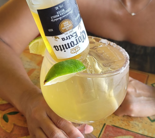 A large margarita glass with a beer bottle upside down, garnished with lime wedges and a salted rim.