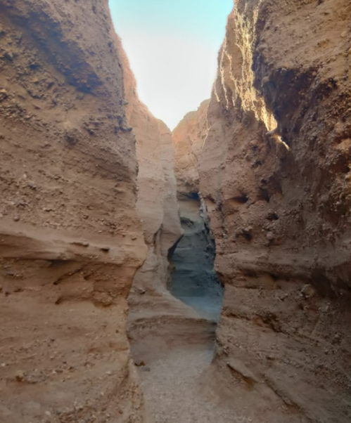 Narrow canyon with steep, textured walls and bright light at the end, creating a dramatic natural pathway.