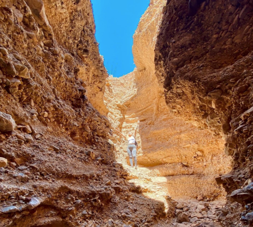 A person climbs a rocky canyon with steep, textured walls under a clear blue sky.