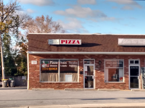 A brick building with a pizza shop and a boutique, featuring signs for pizza, subs, steaks, and pastries.