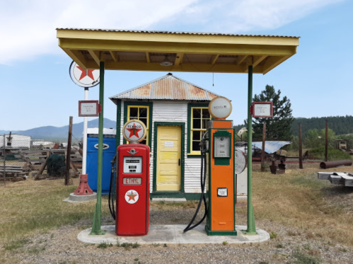 Vintage gas station with red and orange pumps, a yellow roof, and a small white building in a rural setting.