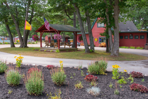 A red building with a gazebo and flowers, surrounded by trees and a winding path in a scenic outdoor setting.