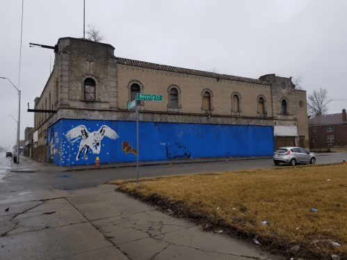 Abandoned building with a blue mural and a white horse, located at the corner of Beverly Lane on a rainy day.