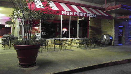 Exterior of High Point Pizza with red and white striped awning, empty outdoor seating, and warm lighting at night.