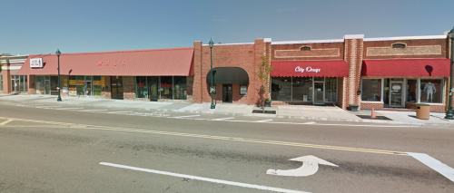 A street view of a brick storefront with red awnings, featuring shops and a clear blue sky above.