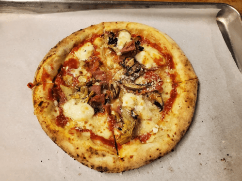 A freshly baked pizza topped with cheese, vegetables, and slices of meat on a parchment-lined tray.