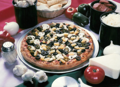 A pizza topped with olives, mushrooms, and pineapple, surrounded by various toppings and ingredients on a table.