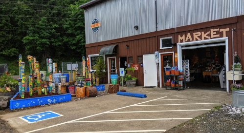 A rustic market building with colorful wooden sculptures outside, featuring a wheelchair-accessible parking space.
