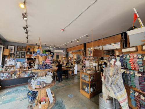 A cozy shop interior filled with various items, including crafts, decor, and textiles, with a customer at the counter.