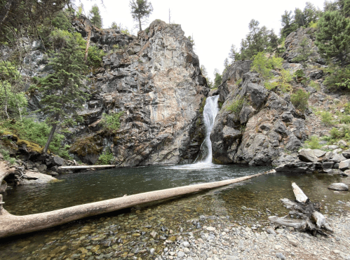 A serene waterfall cascades into a clear pool, surrounded by rocky cliffs and lush greenery.