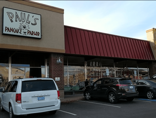 Exterior of Paul's Pancake Parlor, featuring a sign and parked cars in front of a brick building with a red awning.