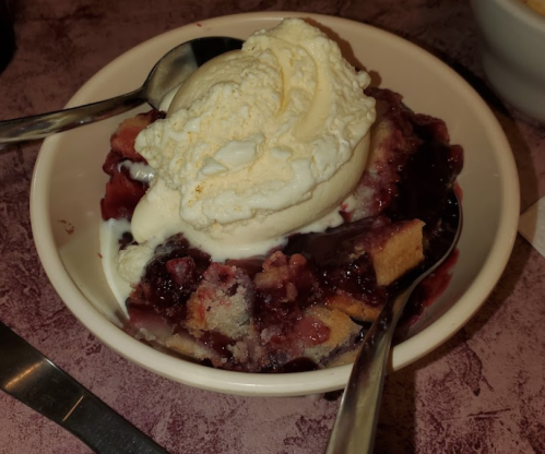 A bowl of dessert featuring cake pieces topped with berry sauce and a scoop of vanilla ice cream. Two spoons are visible.