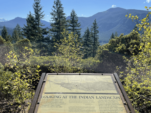 A sign titled "Looking at the Indian Landscape" with mountains and trees in the background under a clear blue sky.