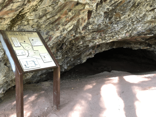 A cave entrance with a sign displaying information about the cave's features and history.