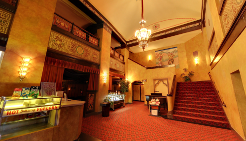 Art Deco-style lobby with ornate decor, a popcorn stand, and a grand staircase leading to an upper level.