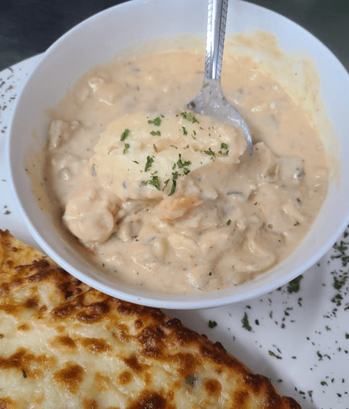 A bowl of creamy seafood chowder with shrimp, served with a cheesy, golden-brown bread on the side.