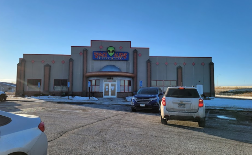 Exterior of a building named "Space Aliens" with a clear blue sky and parked cars in front. Snow on the ground.