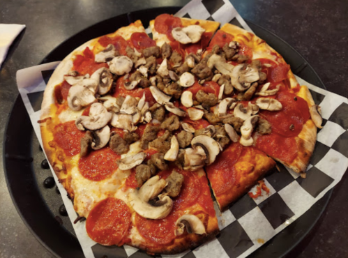 A pizza topped with pepperoni, sausage, and mushrooms, served on a black plate with checkered paper.