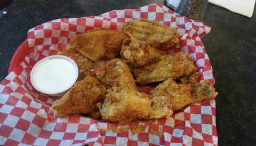 A basket of seasoned fried chicken wings with a side of dipping sauce, served on red and white checkered paper.