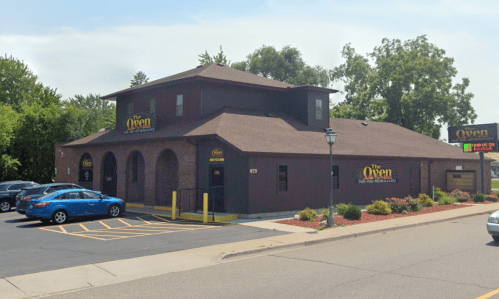 Exterior view of The Oven restaurant, featuring a two-story brick building and parking lot with a blue car.