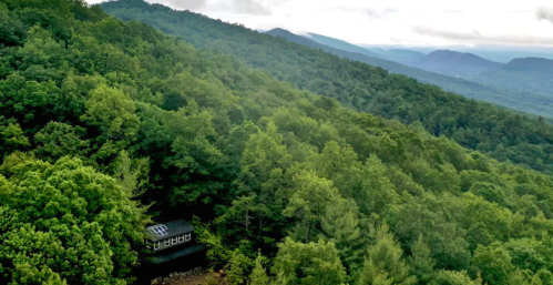 A secluded cabin nestled in lush green mountains, surrounded by dense trees and misty hills in the background.
