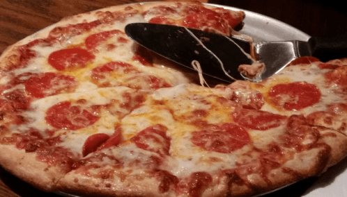 A freshly baked pepperoni pizza with melted cheese, partially sliced and served on a metal tray.