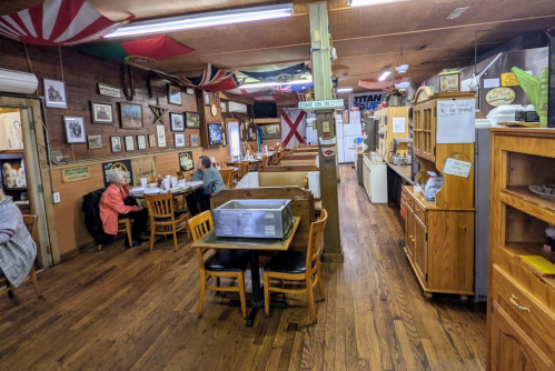 A cozy restaurant interior with wooden tables, flags on the walls, and patrons enjoying their meals.
